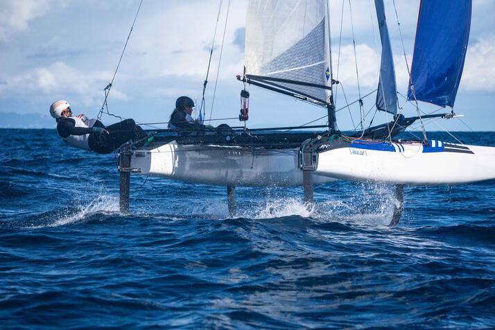 A nacra 17 catamaran sailboat foiling over the water in front of barcelona